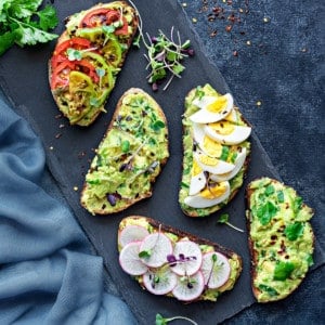 overhead shot of avocado toast with different topping ideas - boiled egg, sliced radishes, and tomatoes