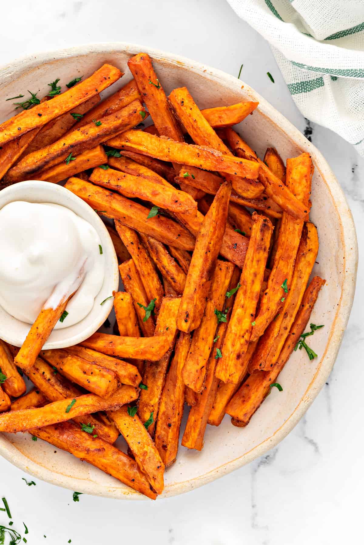 close up overhead shot of air fryer baked sweet potato fries in an earthenware bowl with a small dipping bowl of sauce