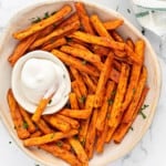 baked sweet potato fries in a cream colored bowl with a small dipping bowl of aioli
