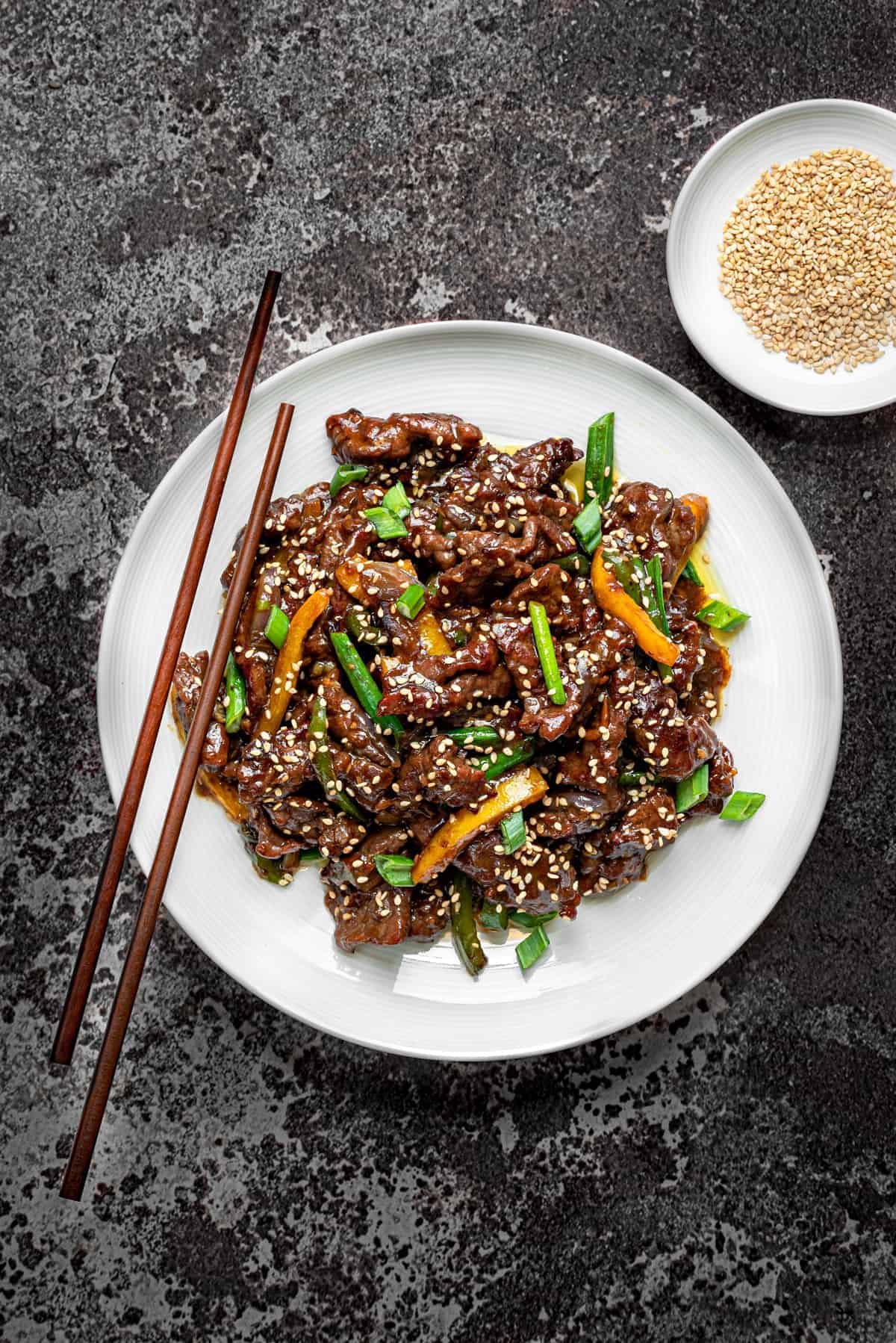 Chinese Beef stir fry in a white bowl with wooden chopsticks on a grey background