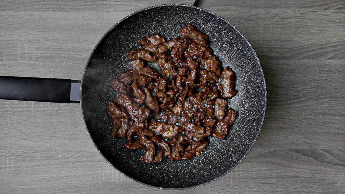 beef being stir fried in wok with ginger and garlic
