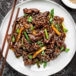 Chinese Beef stir fry in a white pasta bowl with wooden chopsticks on a grey background