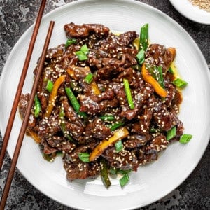 Chinese Beef stir fry in a white pasta bowl with wooden chopsticks on a grey background