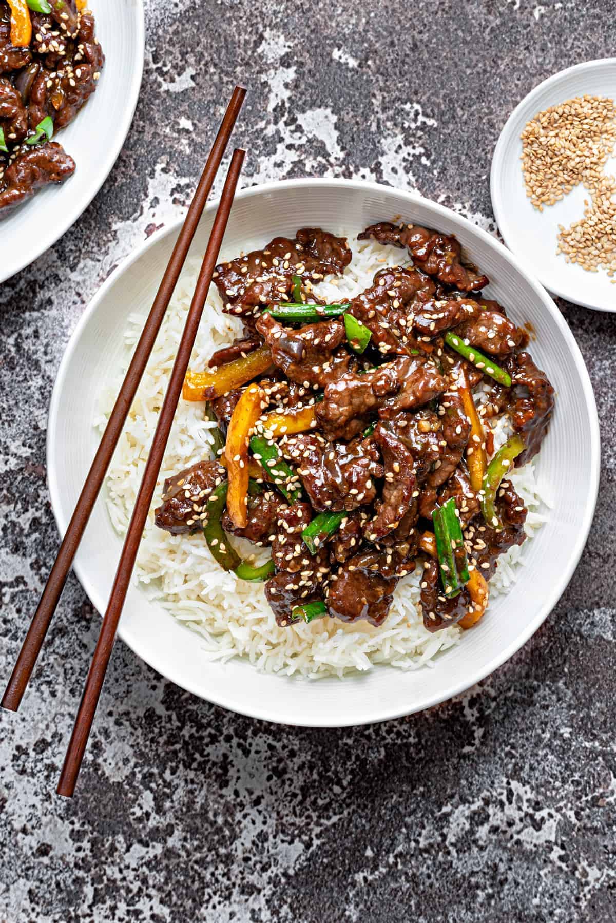 Chinese style beef stir fry over white rice in a white bowl with wooden chopsticks