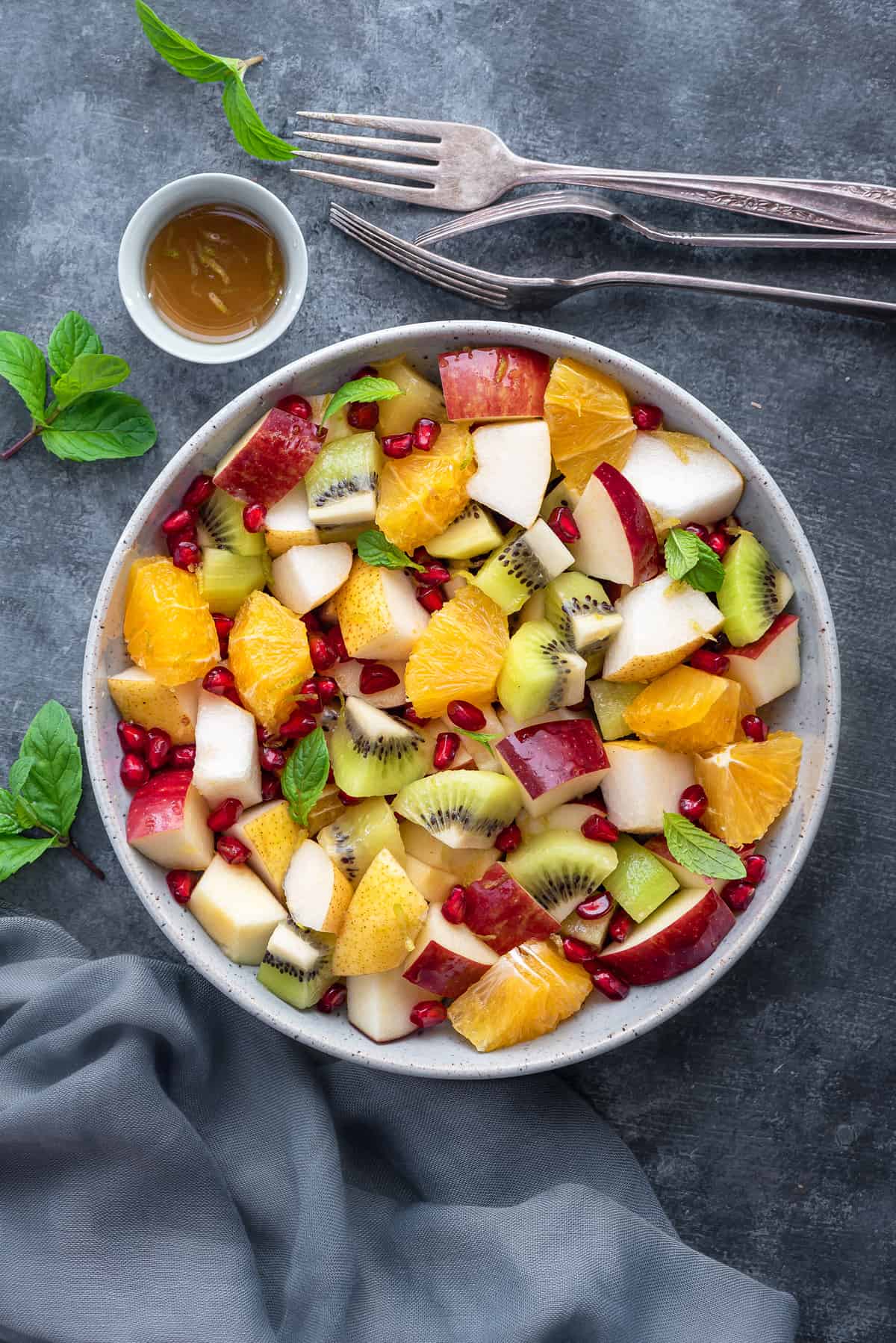 overhead shot of winter fruit salad in a white bowl on a grey table with fresh mint leaves