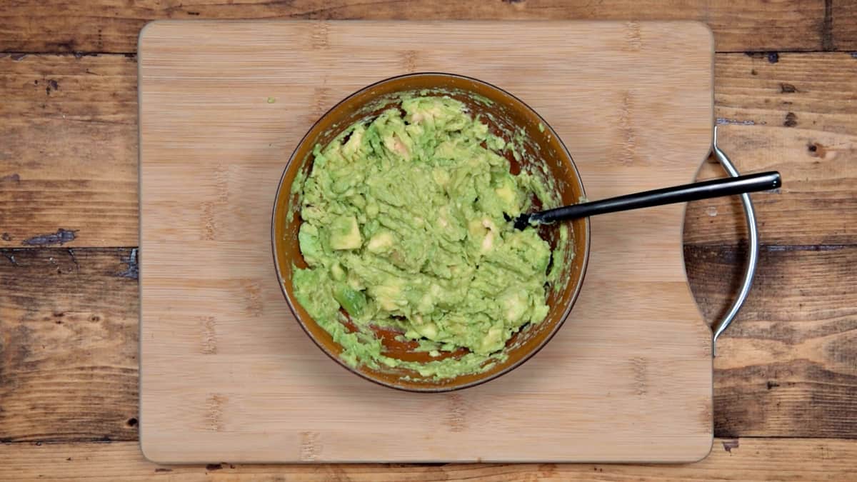 avocado that has been mashed with a fork in a brown bowl