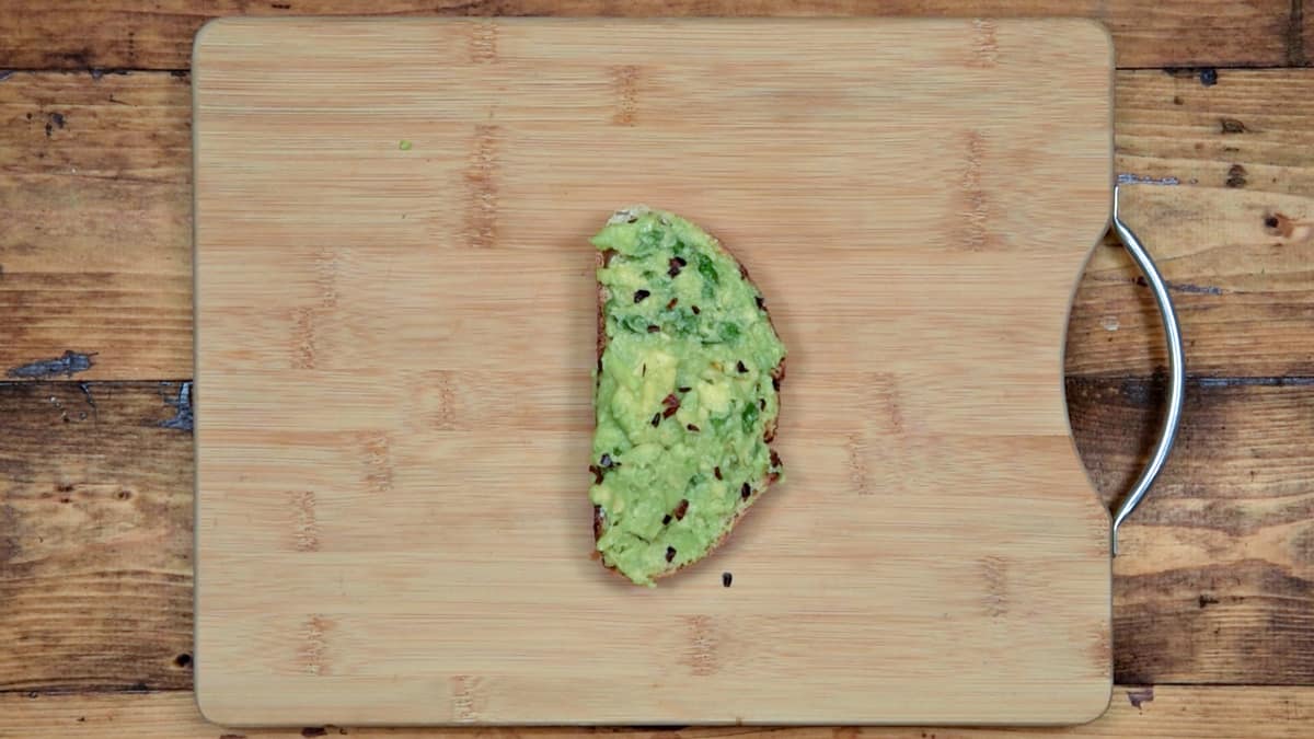 avocado on toast sprinkled with dried chili flakes placed on a wooden cutting board