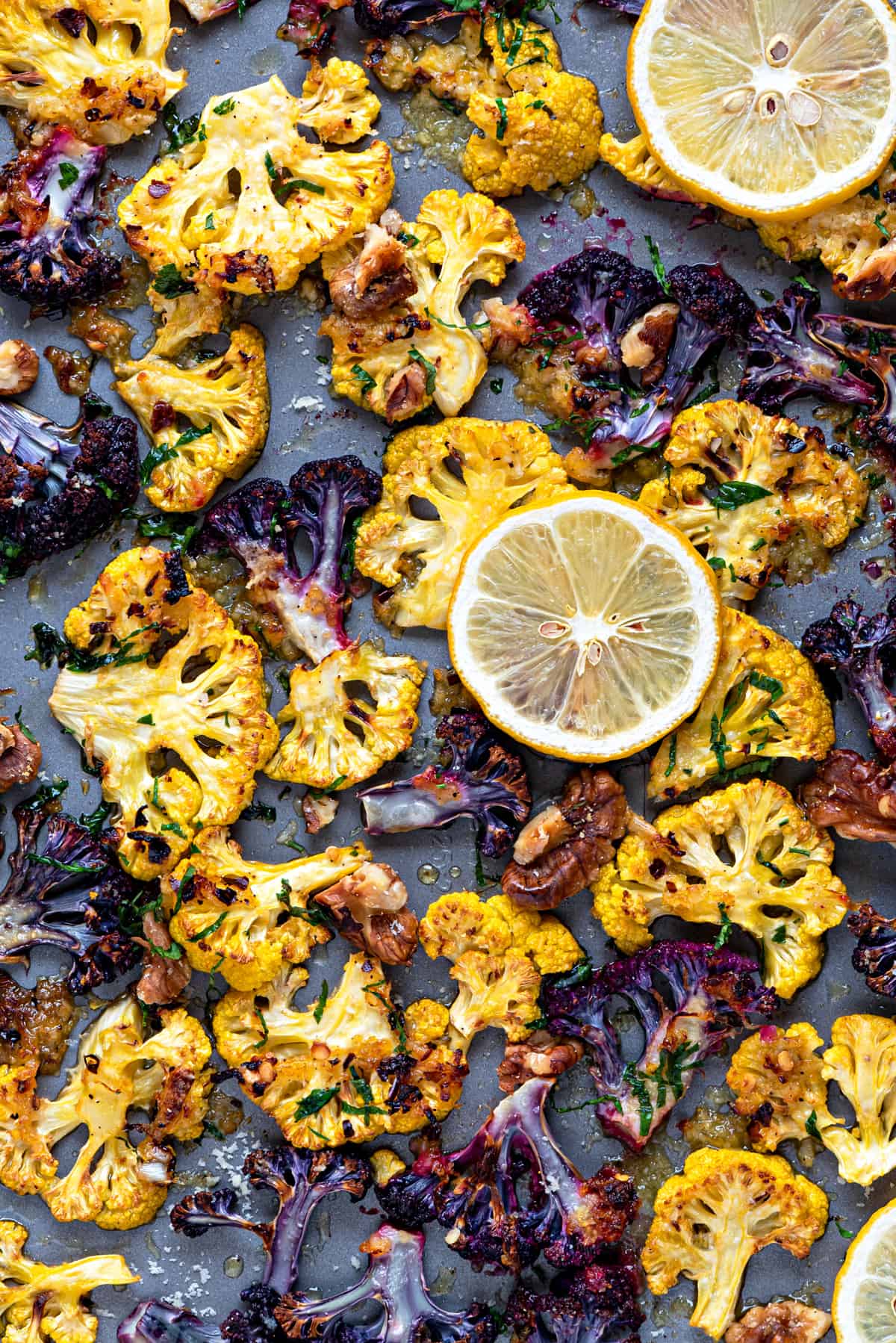 close up shot of orange and purple roasted cauliflower parmesan on a sheet pan with walnuts