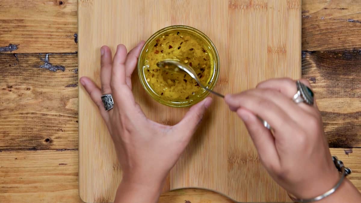 hands mixing together the olive oil, garlic and red pepper flakes dressing in a small bowl
