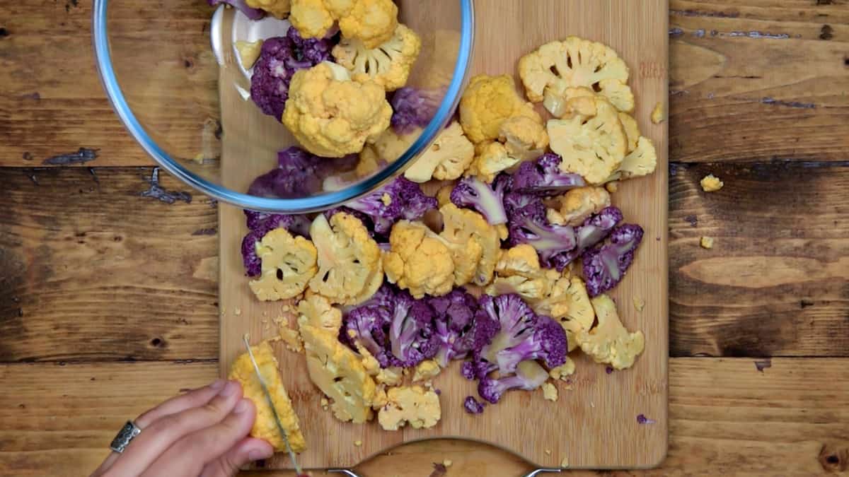 hand slicing ½" slices of orange and purple cauliflower florets on a wooden cutting board