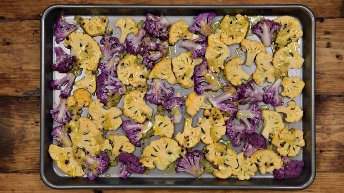 orange and purple cauliflower floret slices on a sheet pan drizzled with red pepper and garlic dressing