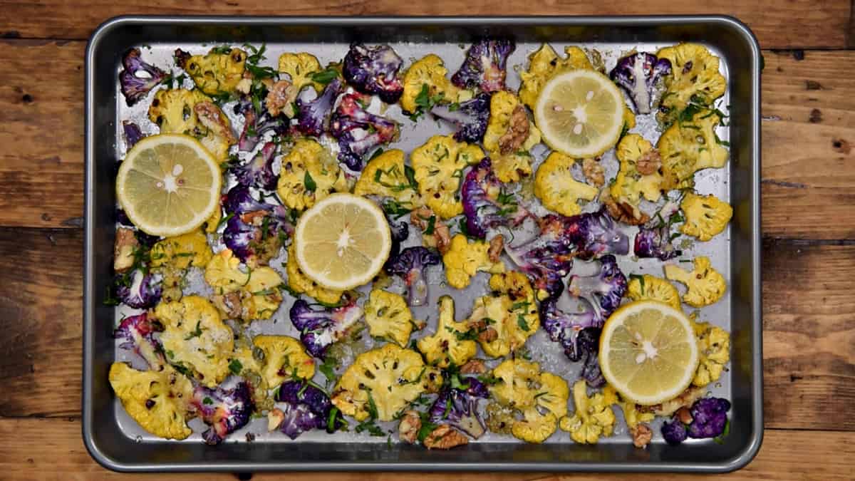 colored cauliflower florets after first bout of roasting topped with lemon slices, parmesan, parsley and walnuts