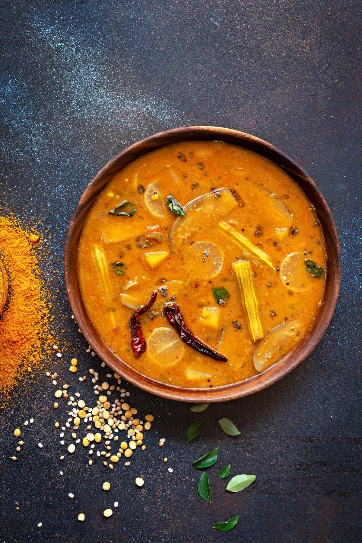 vegetable sambar dal served in wooden bowl, some spices and lentils spread around