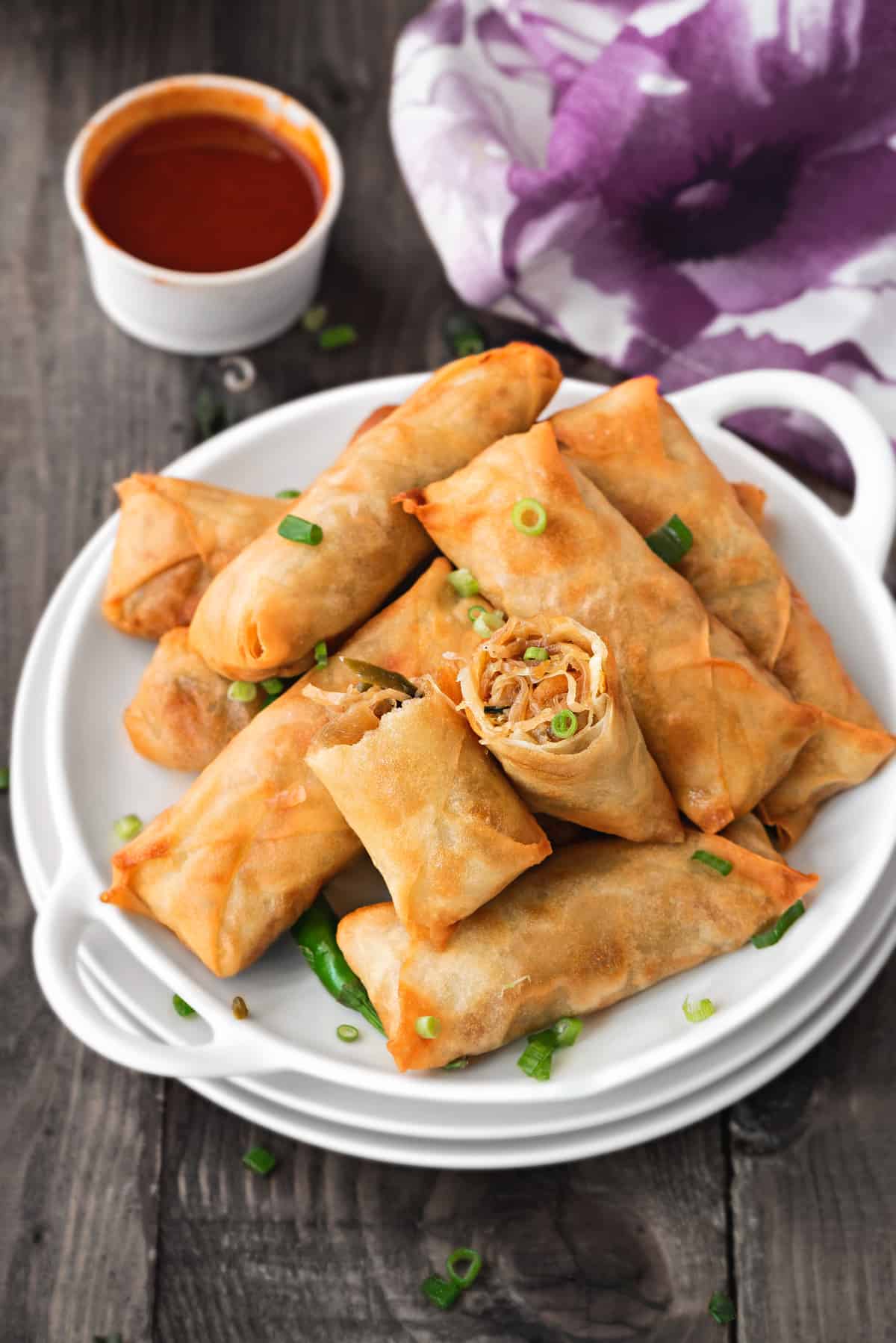 Pile of vegetable spring rolls on a white plate garnished with green onions