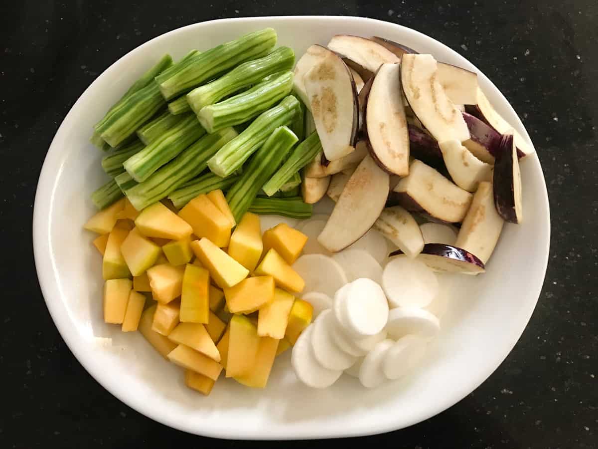 Sliced eggplant, cubed pumpkin, sliced radish and cut vegetable drumsticks placed in white oval plate