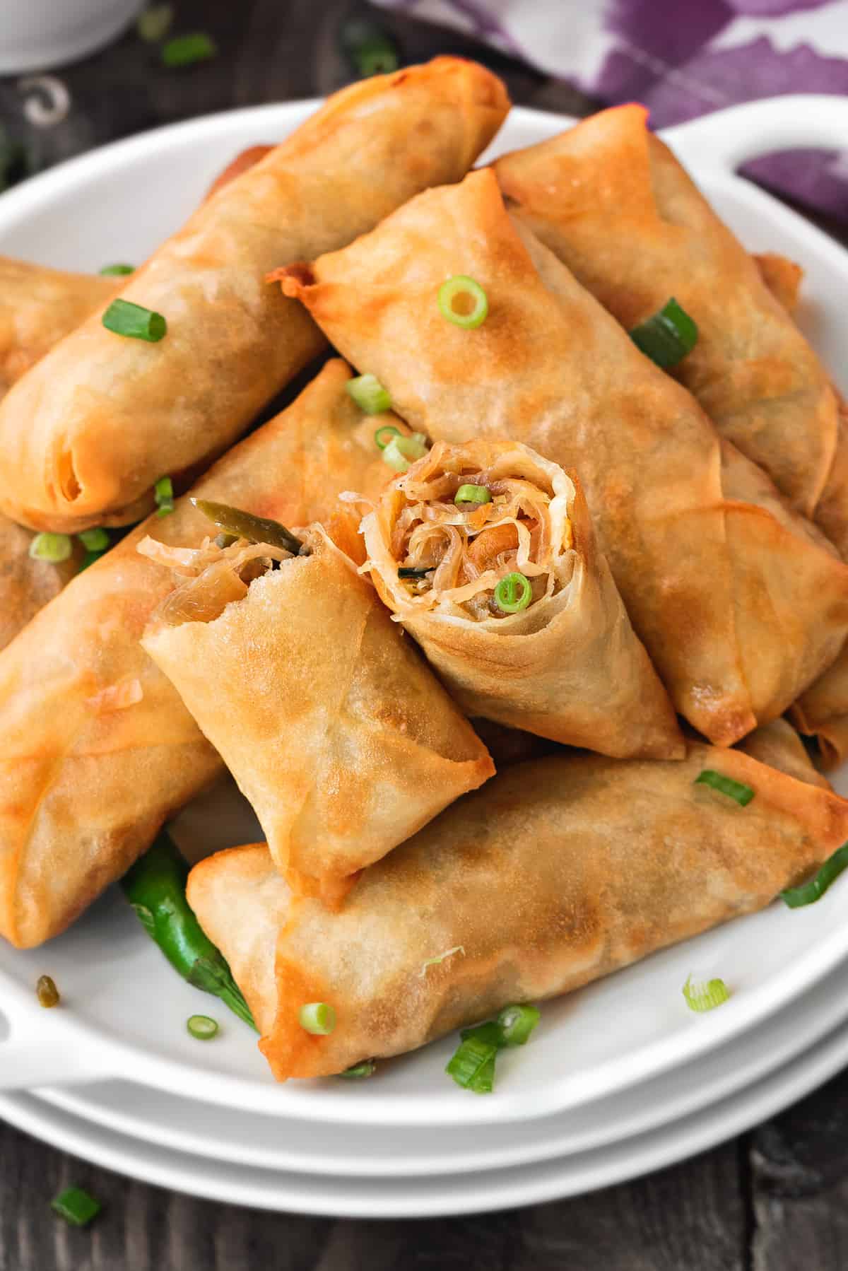 pile of homemade vegetable spring rolls with one broken open to show the filling
