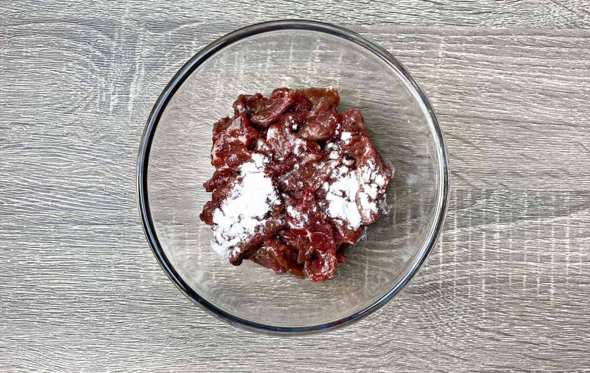 clear glass bowl with beef and sodium bicarbonate to velvet the beef