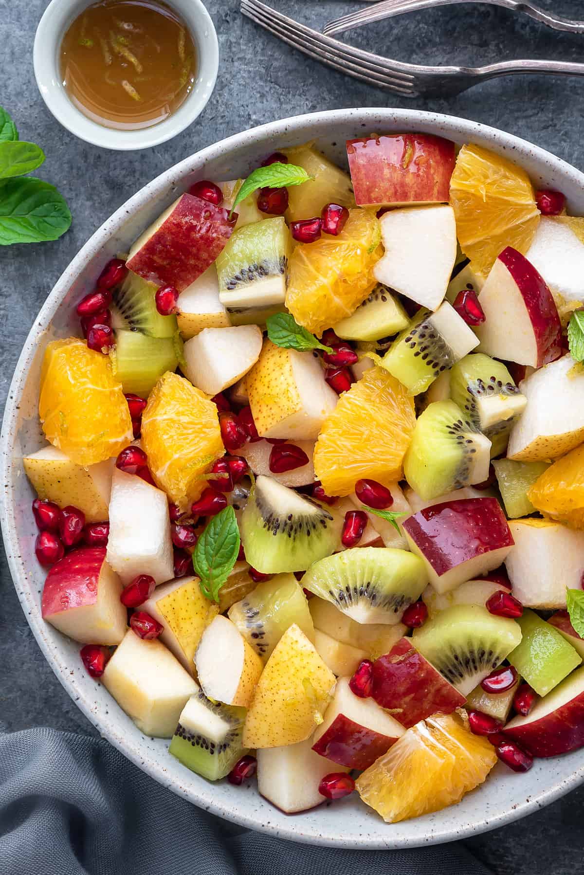 Close up shot of winter fruit salad garnished with fresh mint leaves in a white bowl