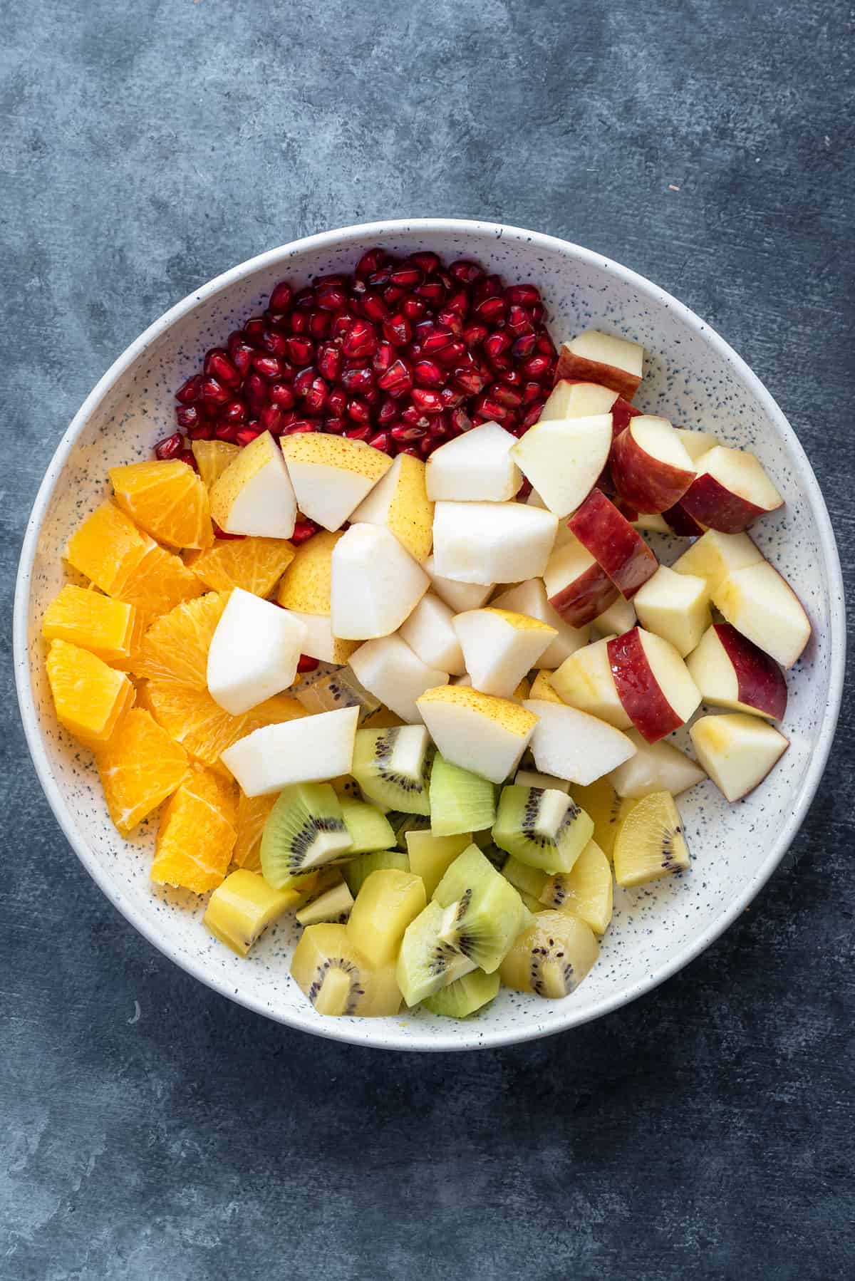 pomegranate arils, orange, pear, apple and kiwi cubes in a white speckled serving bowl