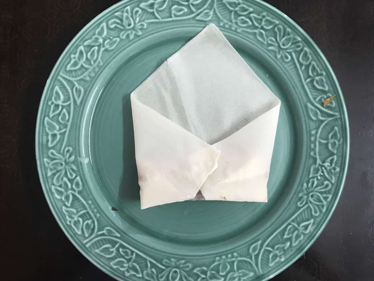 side corners of spring roll wrapper folded in over first roll to look like an open envelope