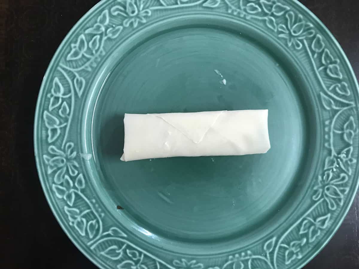 completed vegetarian spring roll on a blue plate prior to frying