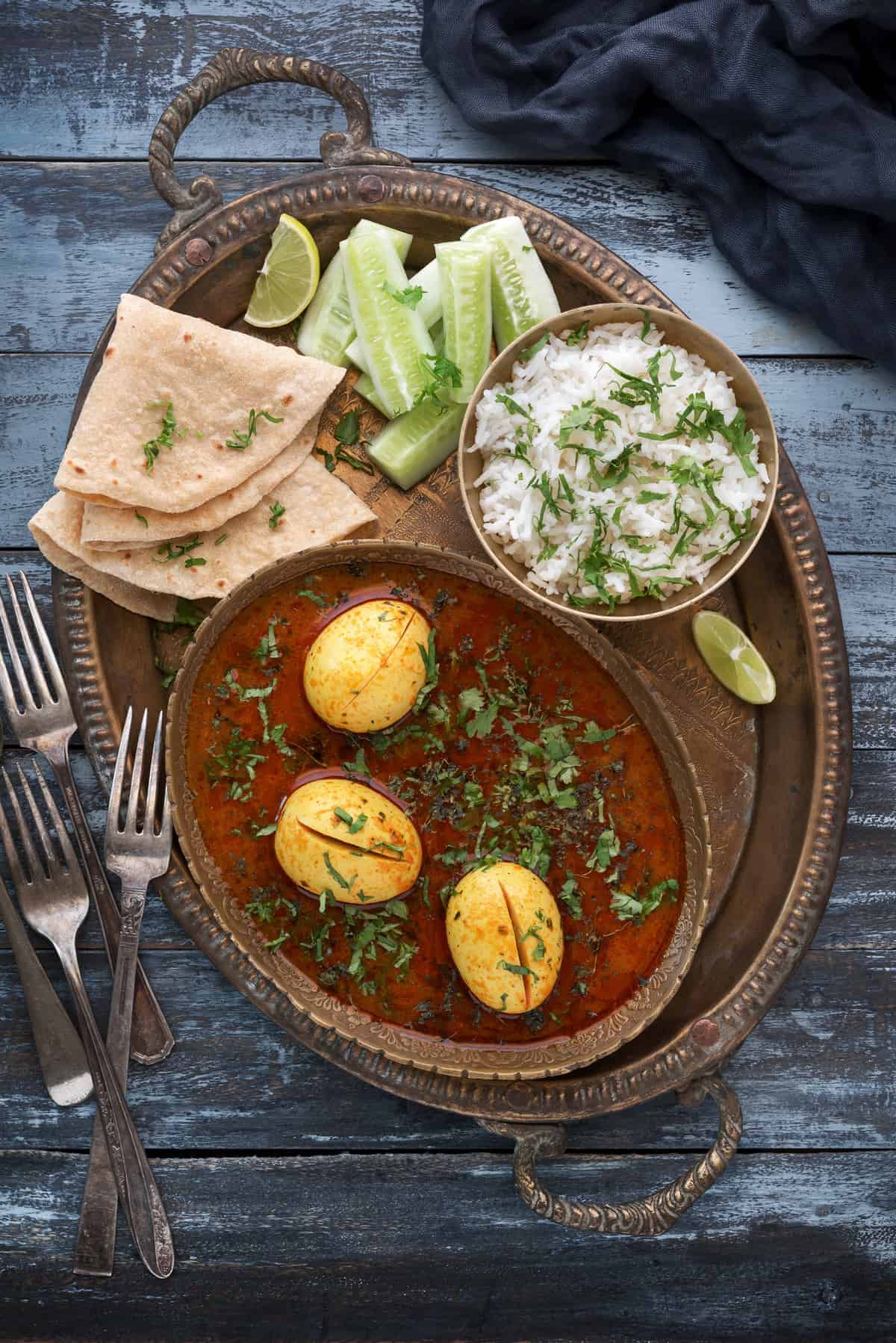 Egg curry placed in oval dish and served along with rice, chapathi and salad on side