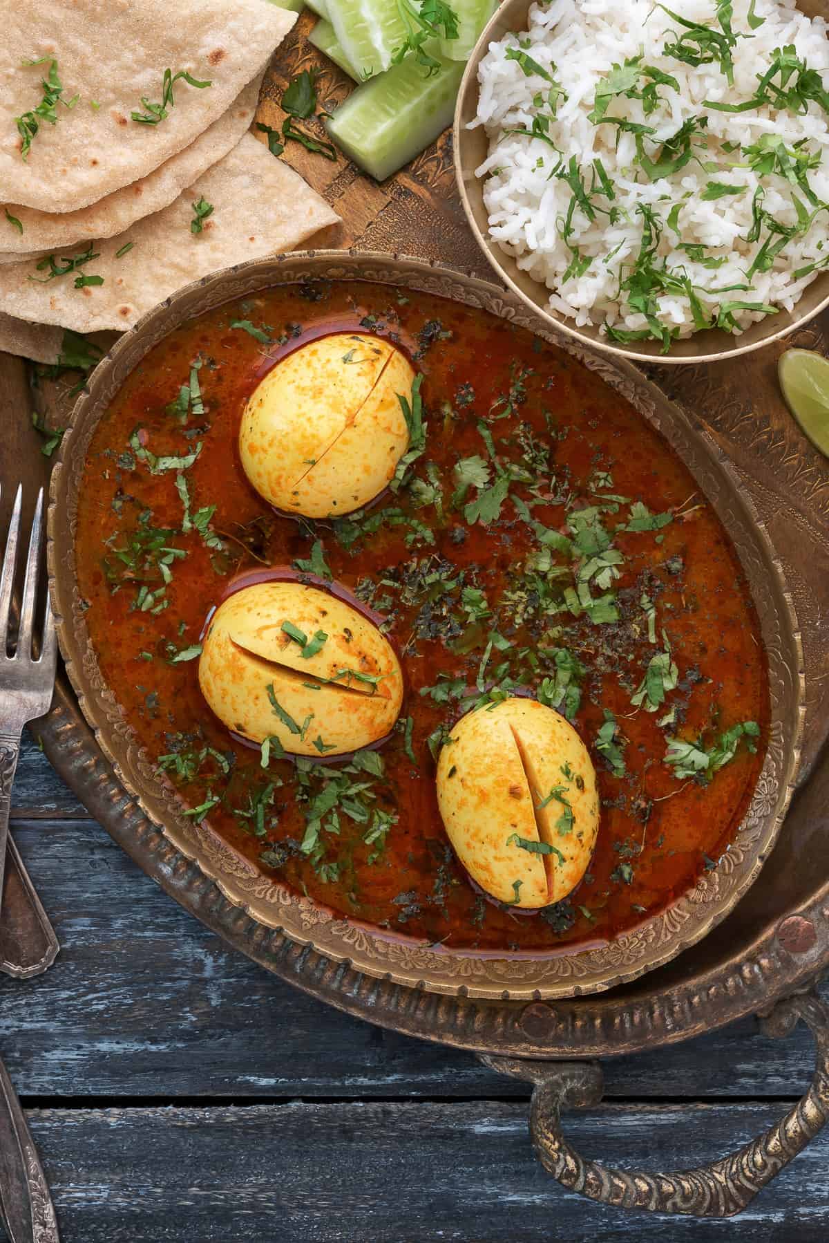 Indian egg curry in tomato onion gravy served with a side of paratha and rice.