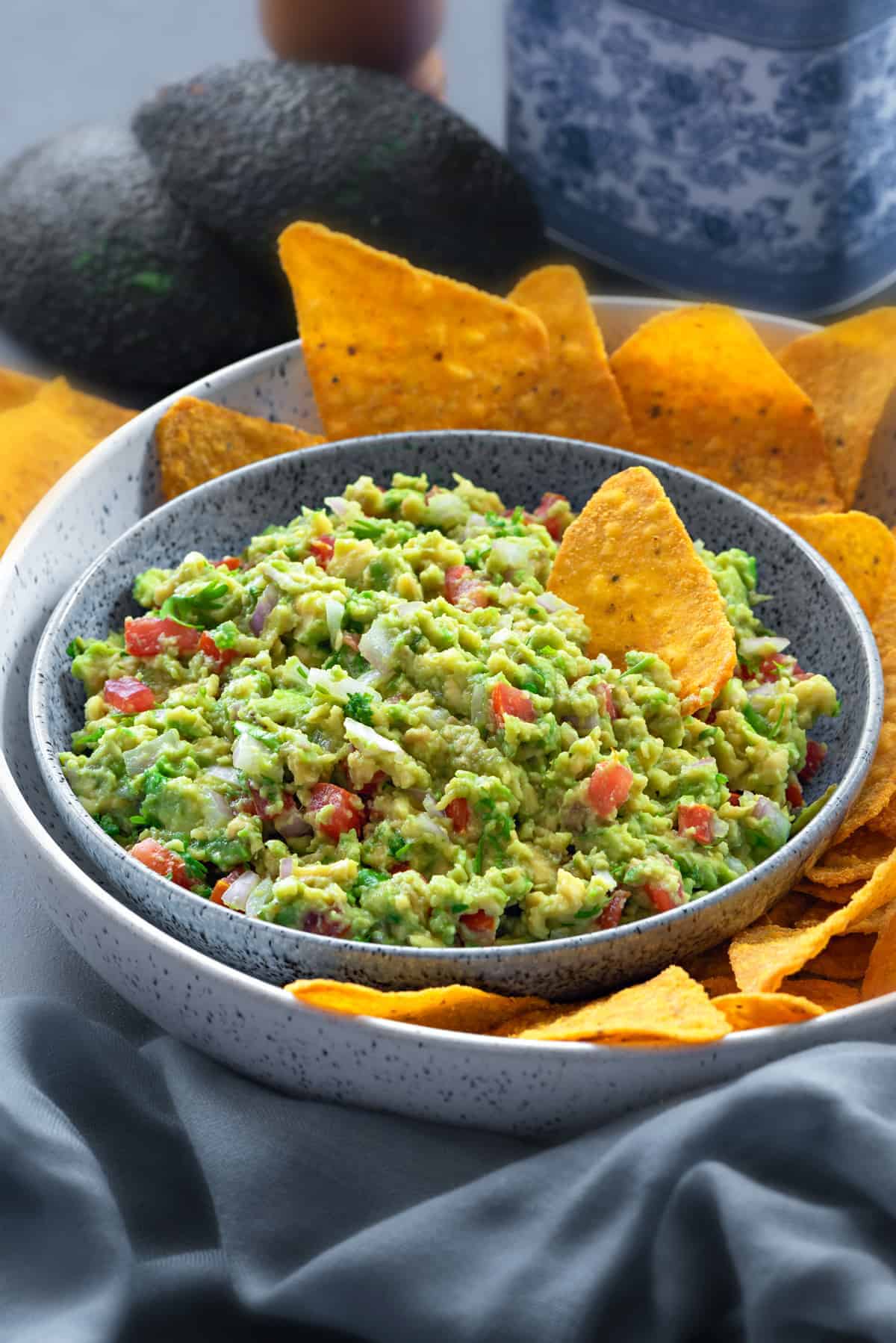 close up of a bowl filled with homemade guacamole with a platter of yellow tortilla chips