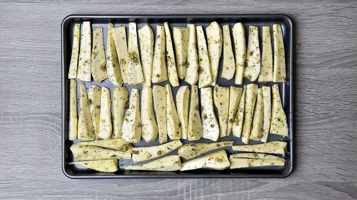 parsnip batons lined up in neat rows on a baking sheet for roasting