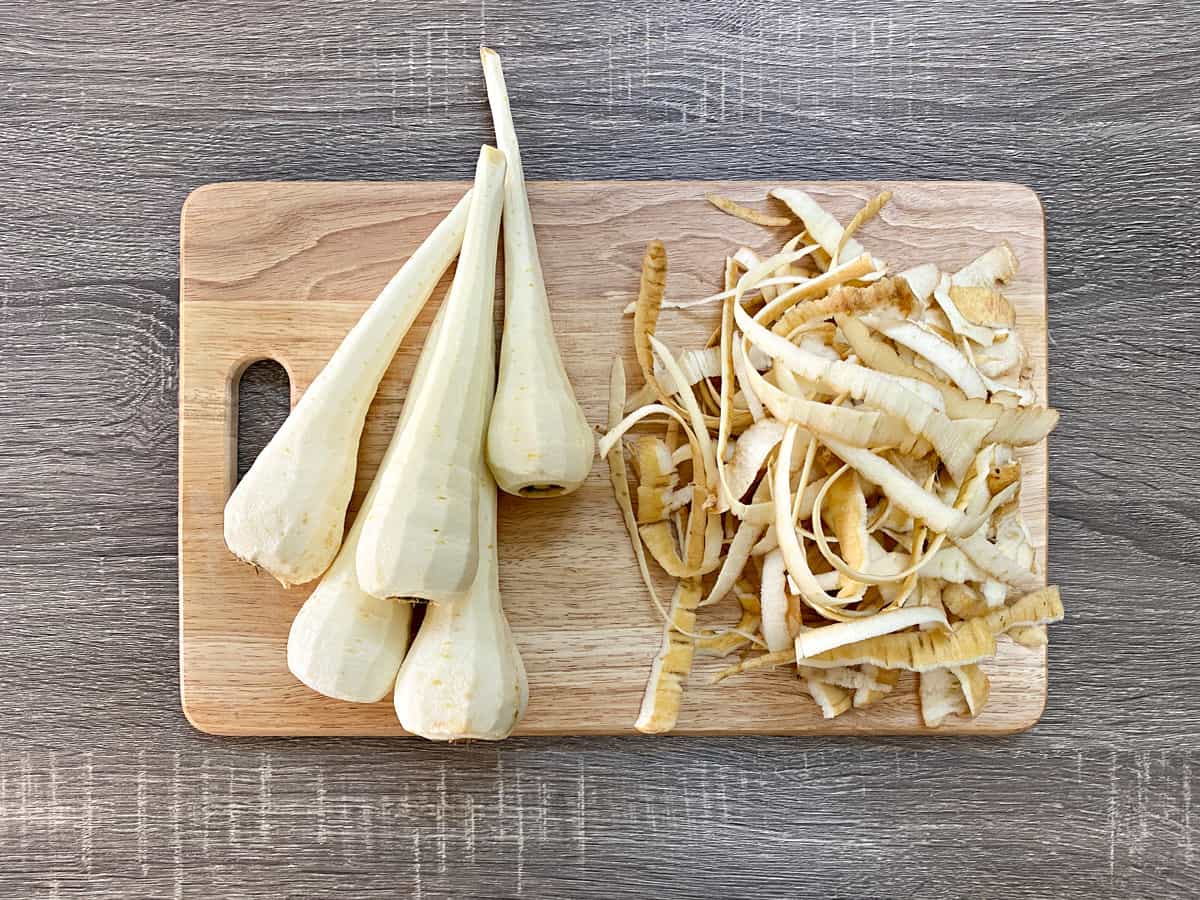 peeled parsnips on a wood cutting board next to peels