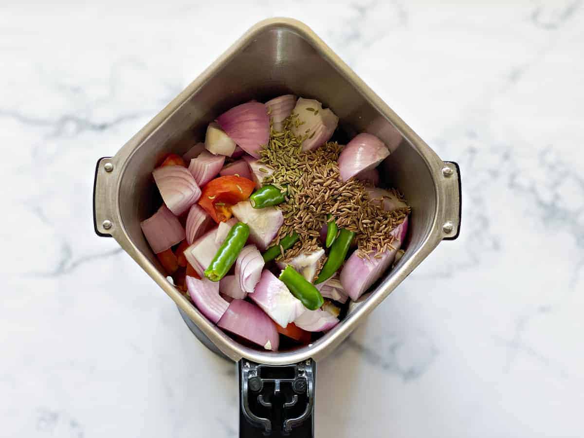 onions, tomatoes, green chiles, fennel seeds, cumin and peppercorn in the base of a grinder