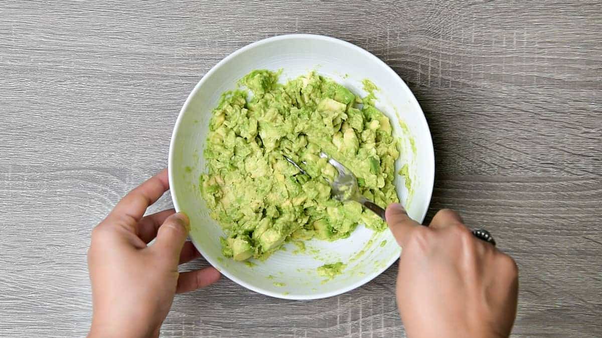 hands using a fork to mash avocado chunks