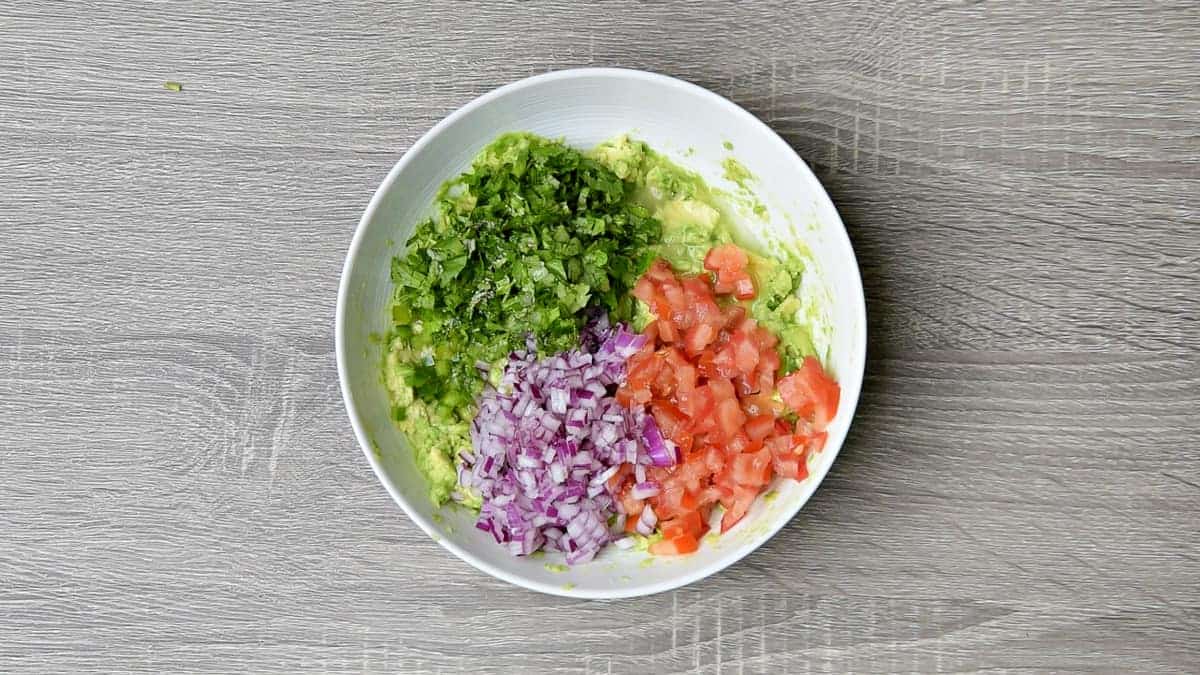 cilantro, red onion and tomato added to bowl with mashed avocado