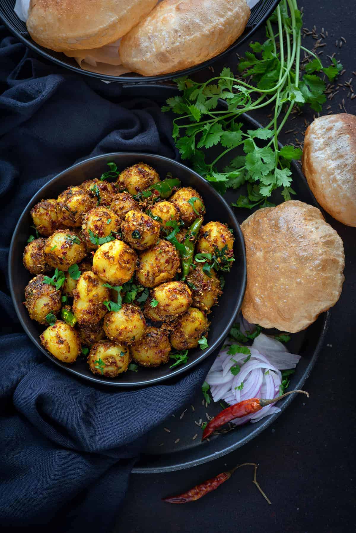 overhead shot of cumin potatoes serving on black plate with fried poori bread on the side