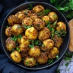 Close up shot of dry jeera aloo masala served in black plate.