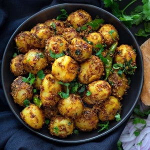Close up shot of dry jeera aloo masala served in black plate.