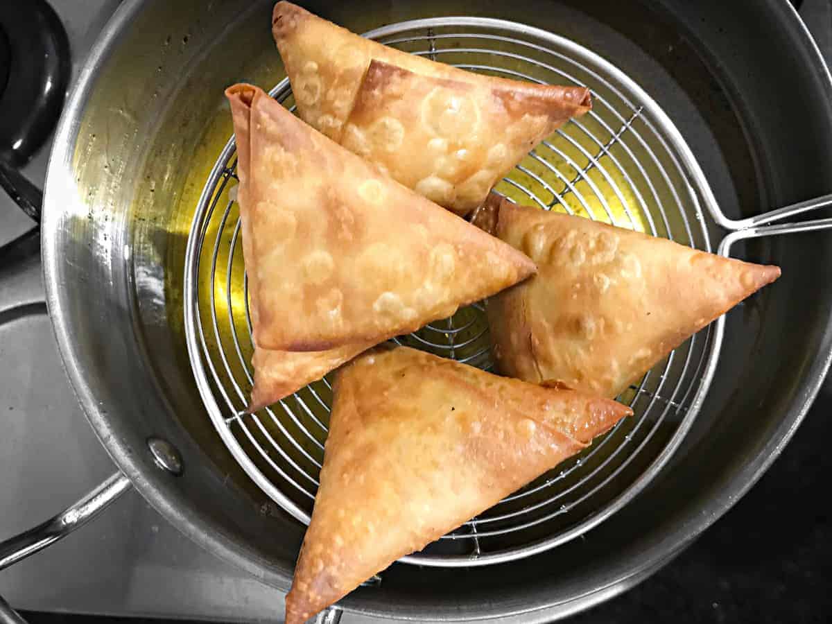 ladle lifting 4 fried keema samosa out of frying oil