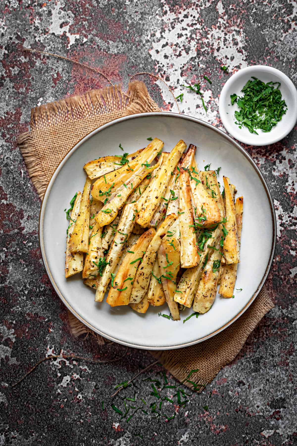 golden brown roasted parsnip batons on a white plate with fresh parsley garnish