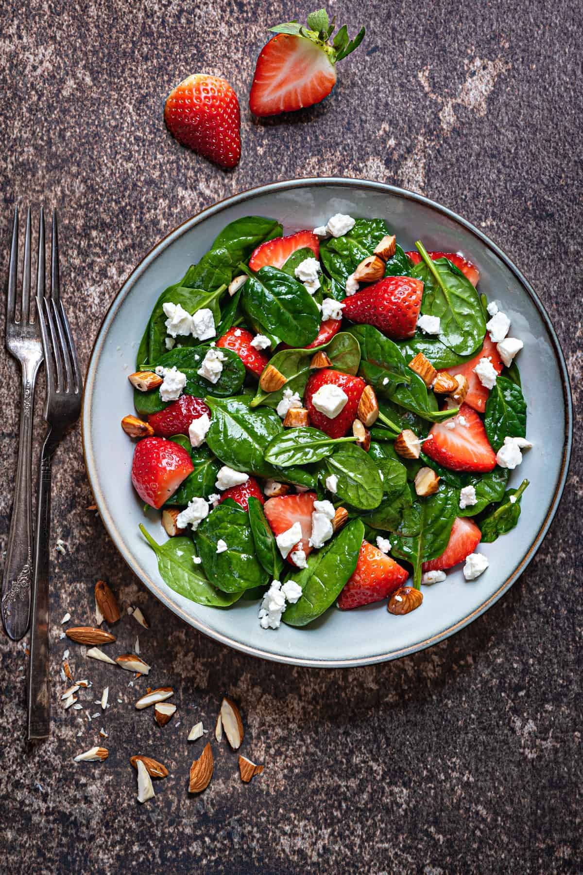 overhead shot of glazed earthenware bowl with strawberry spinach salad with almonds and feta cheese