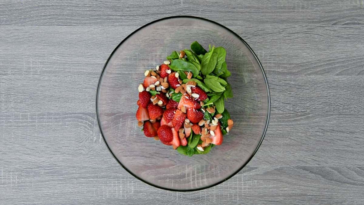 sliced strawberries, chopped almonds and fresh spinach leaves added to bowl with dressing