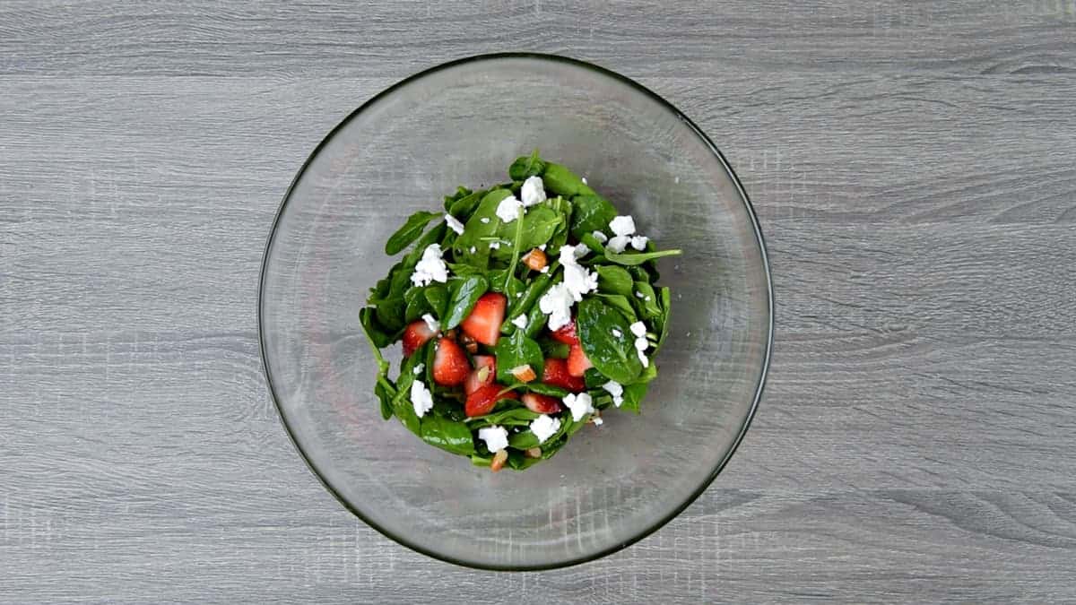 tossed strawberry spinach salad in mixing bowl topped with feta cheese crumbles