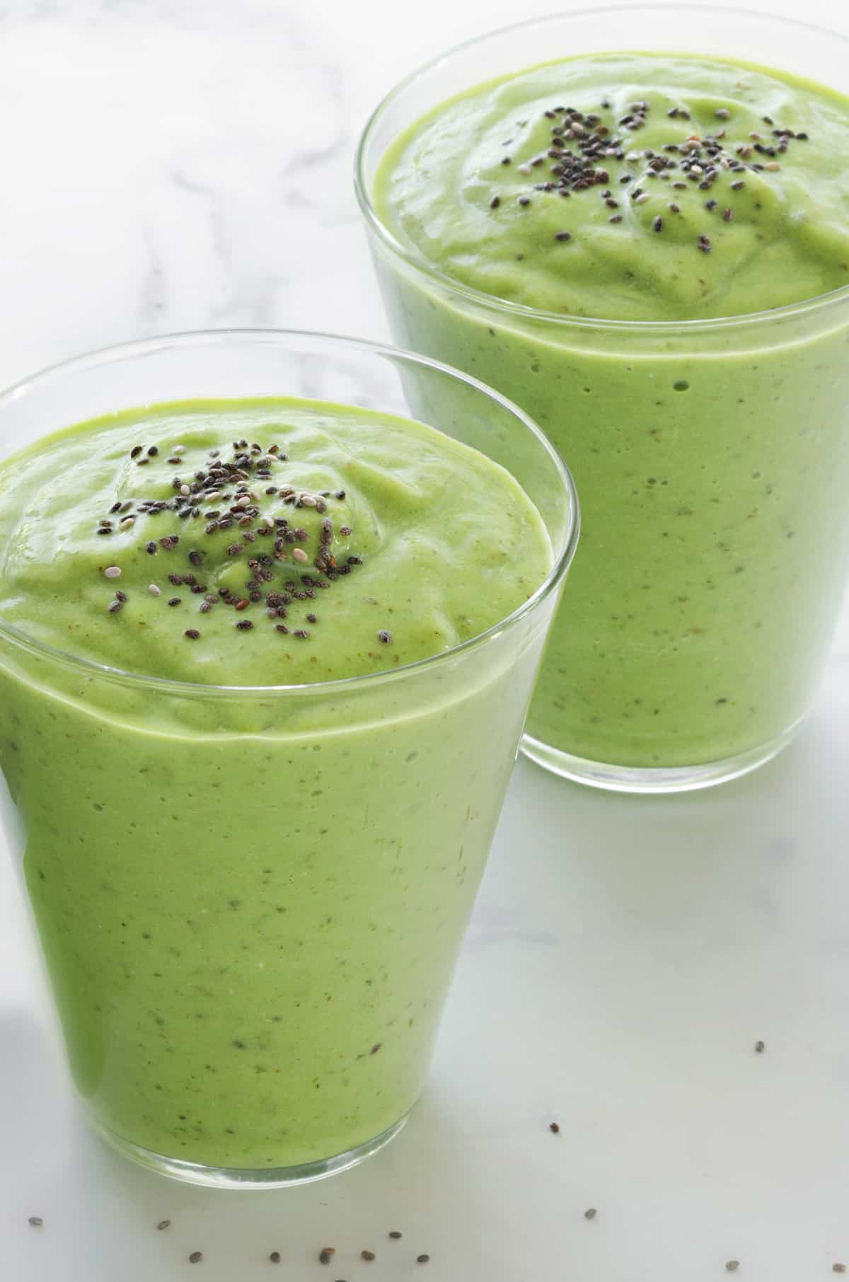two green smoothies made with avocado and spinach placed on a white table