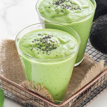 two glasses of healthy green smoothies topped with chia seeds with avocados in the background