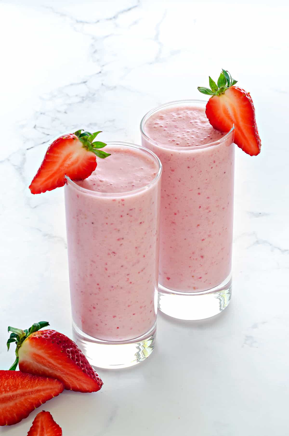 easy strawberry smoothie poured into two tall clear glasses with a fresh strawberry in the foreground