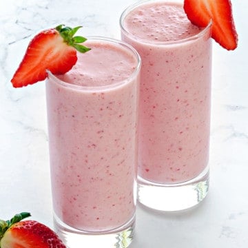 two tall clear collins glasses filled with strawberry smoothie and garnished with fresh strawberry slices