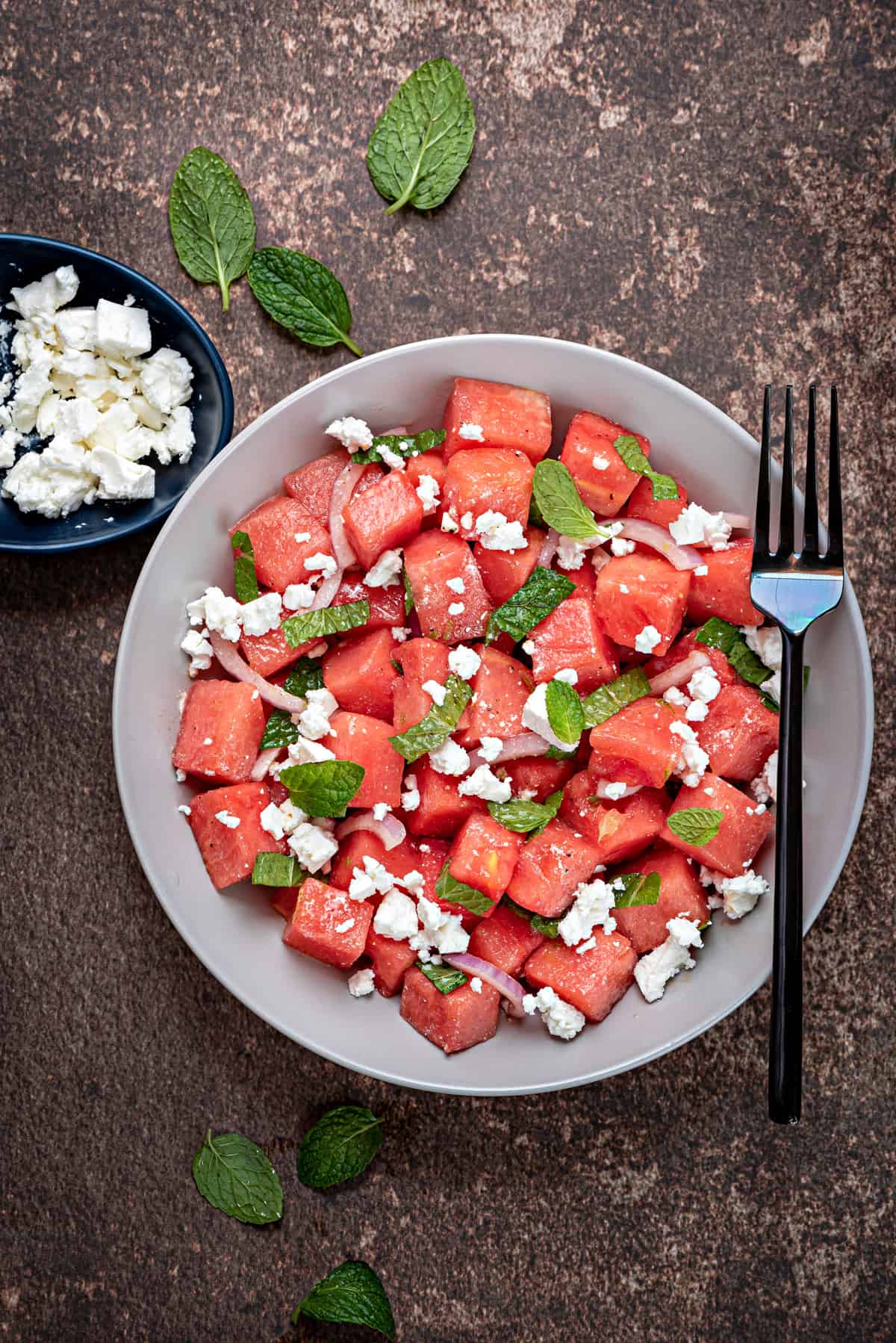 Watermelon feta salad with mint and red onions in a white bowl with a black fork