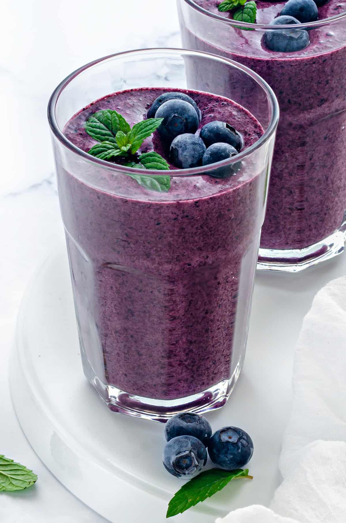 two clear glasses with blueberry smoothie garnished with mint and fresh berries