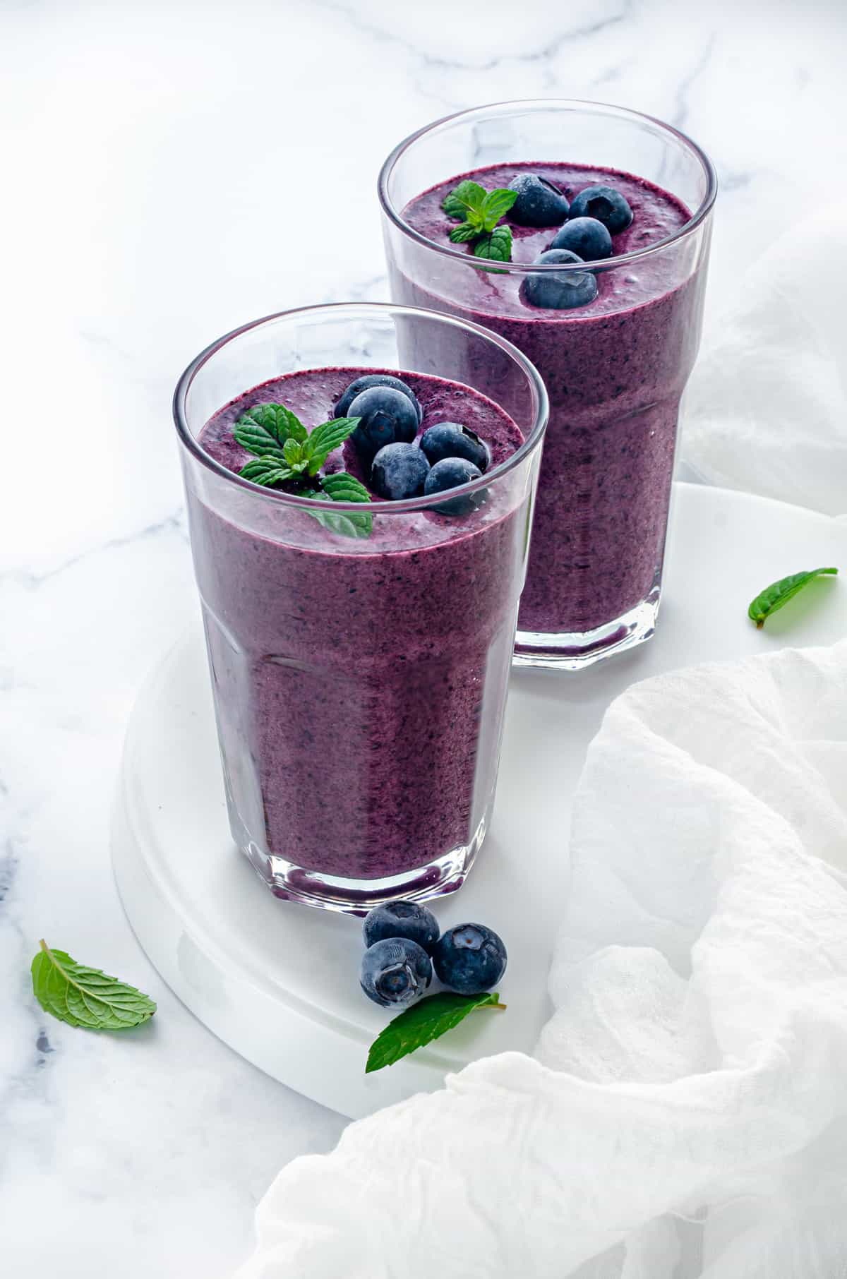 delicious vegan blueberry smoothies on a white table with fresh berries and mint leaves