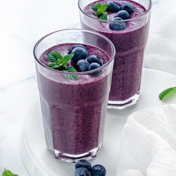 two clear glasses with blueberry smoothie garnished with mint and fresh berries