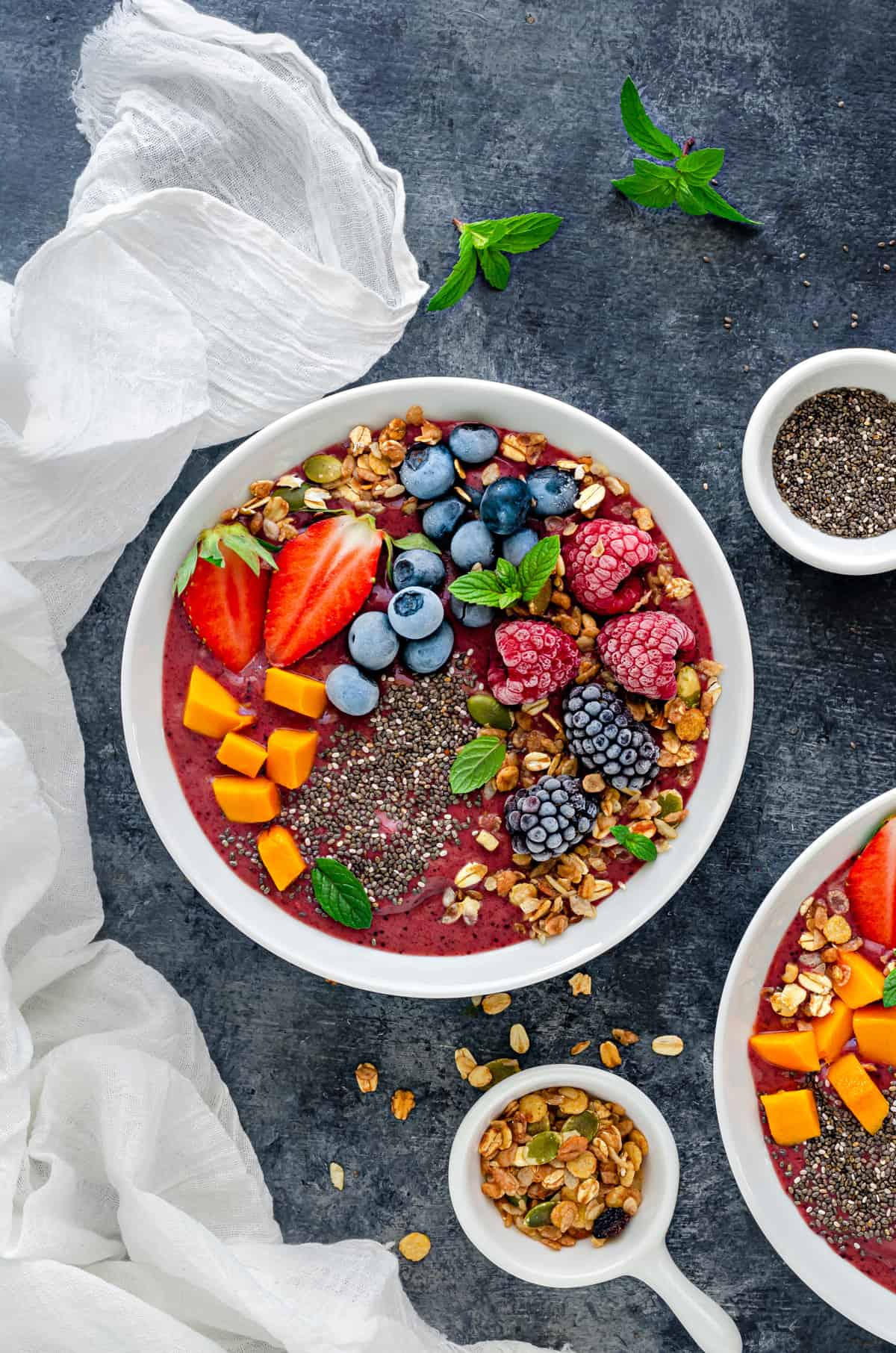 overhead shot of mixed berry smoothie bowl topped with frozen fruit, chia seeds and muesli